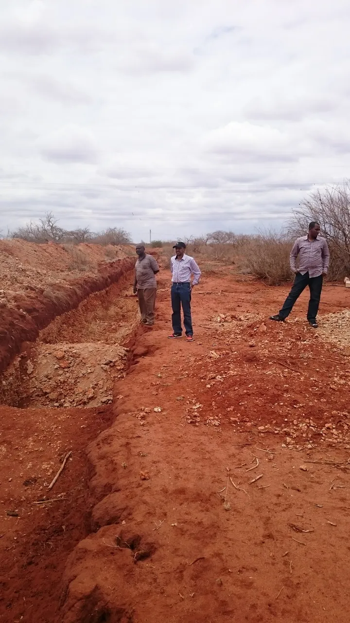 Perimeter trench under construction across red earth
