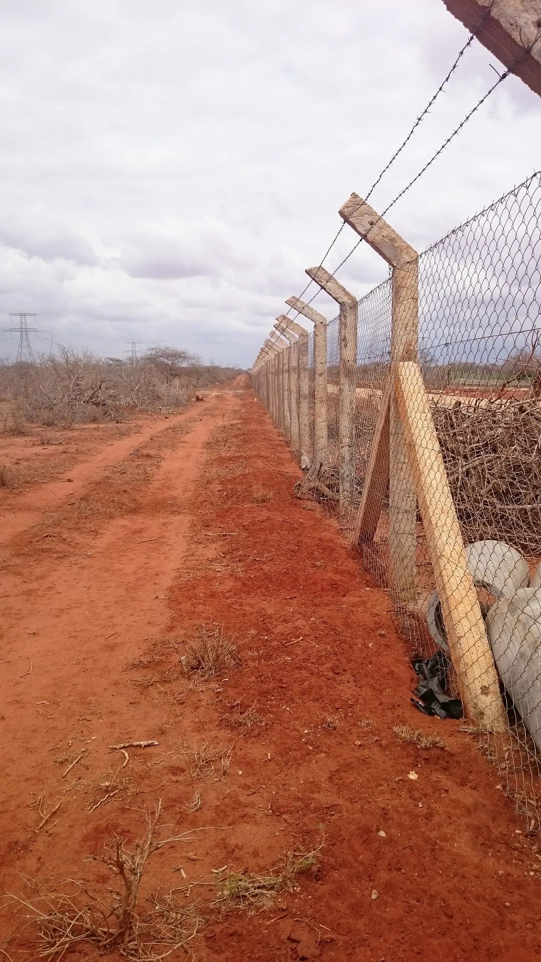 A tall wire perimeter fence beside a red dirt track